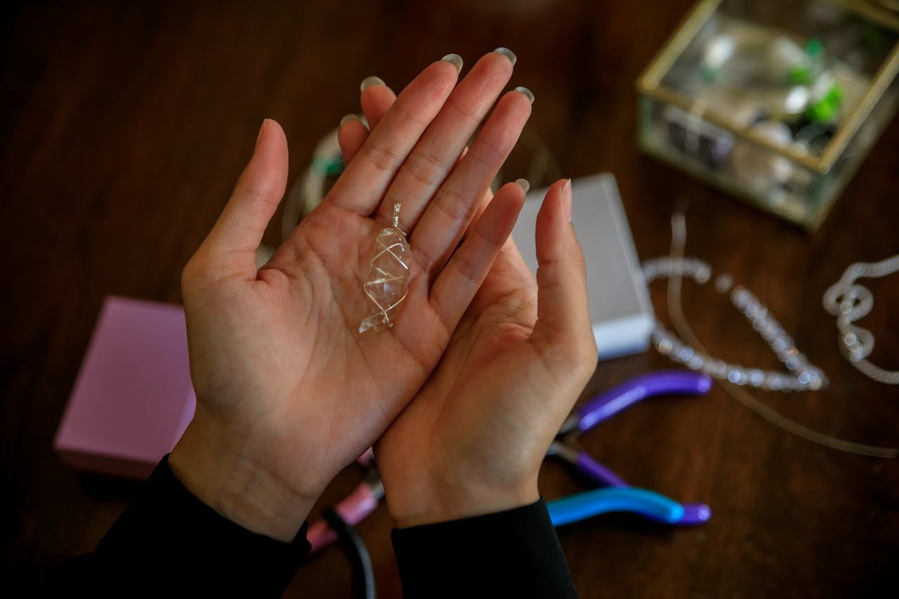 Close-up of hands presenting a handmade silver wire pendant with jewelry tools on a wooden table.